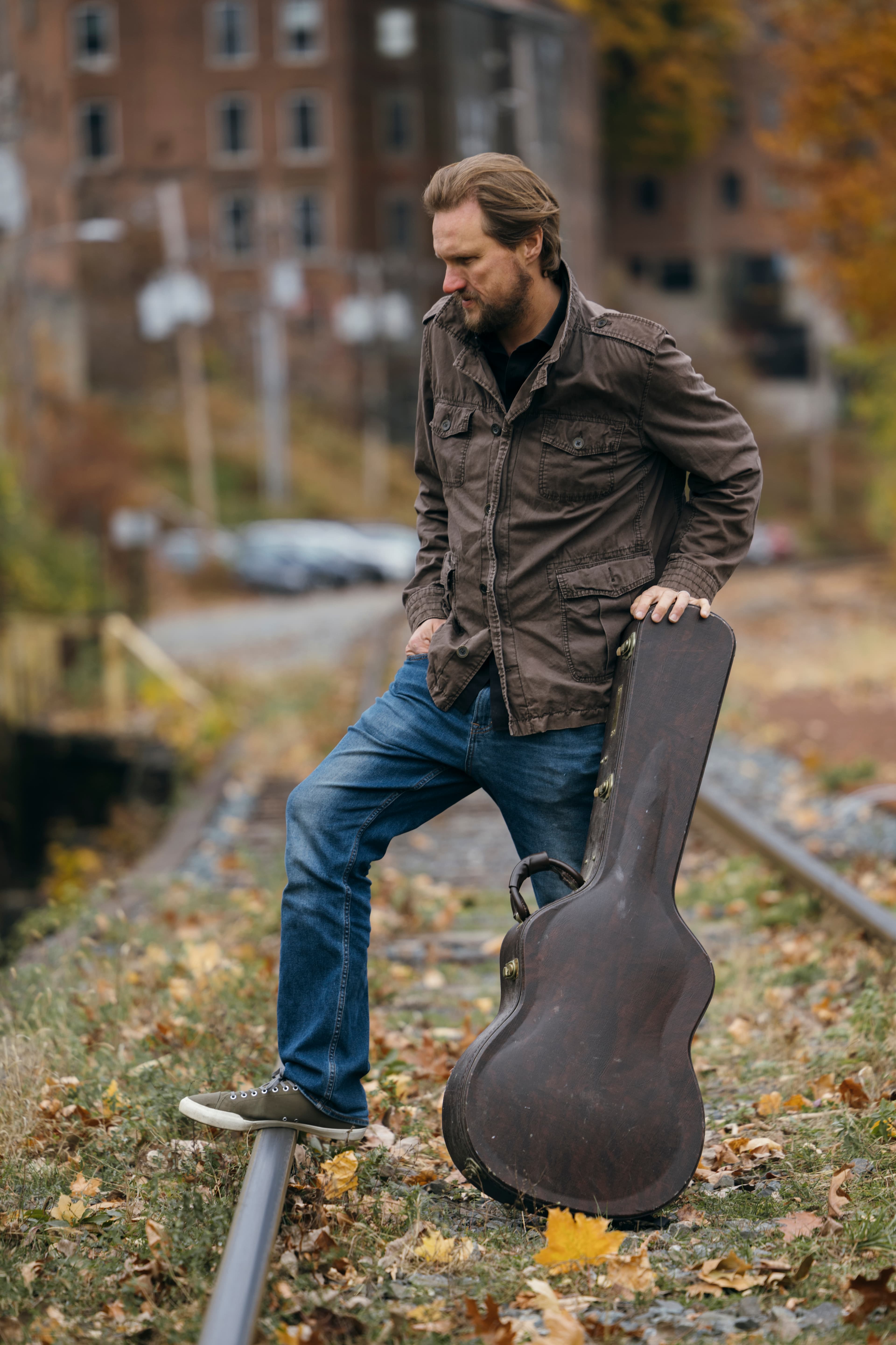 Ian Campbell standing on railroad tracks with a guitar case